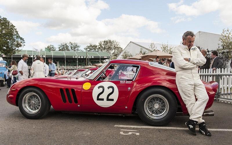 Nick Mason in race suit leaning on his Ferrari 250 GTO at an event