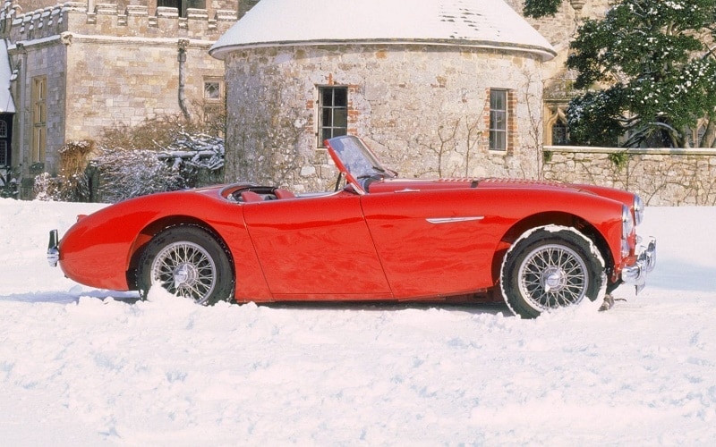 Side view of a red Austin Healey 3000 on the snow-covered compound in a monument