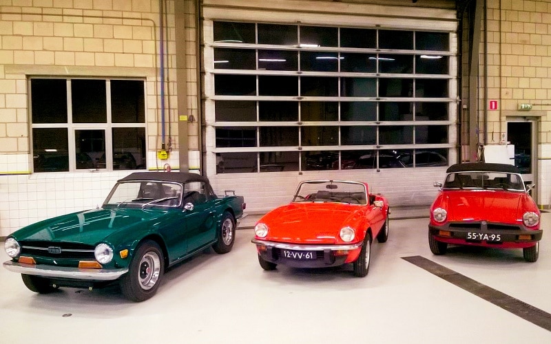 Three classic British sport convertible cars parked side by side in a garage